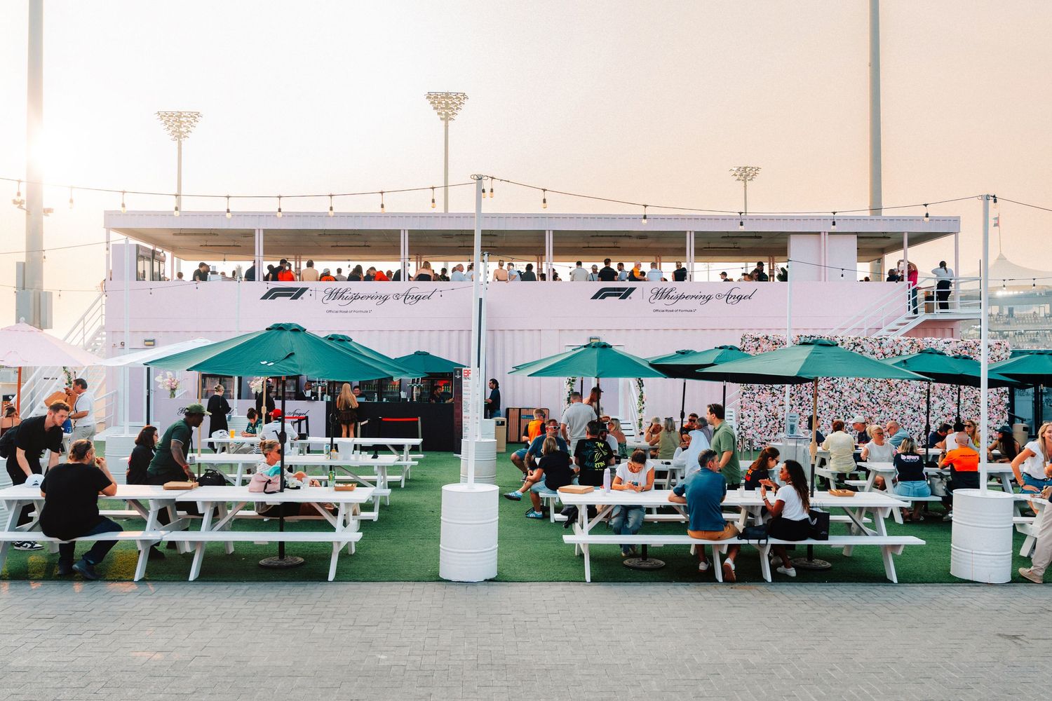 F1 branded outdoor dining area with green umbrellas and white picnic benches at dusk.