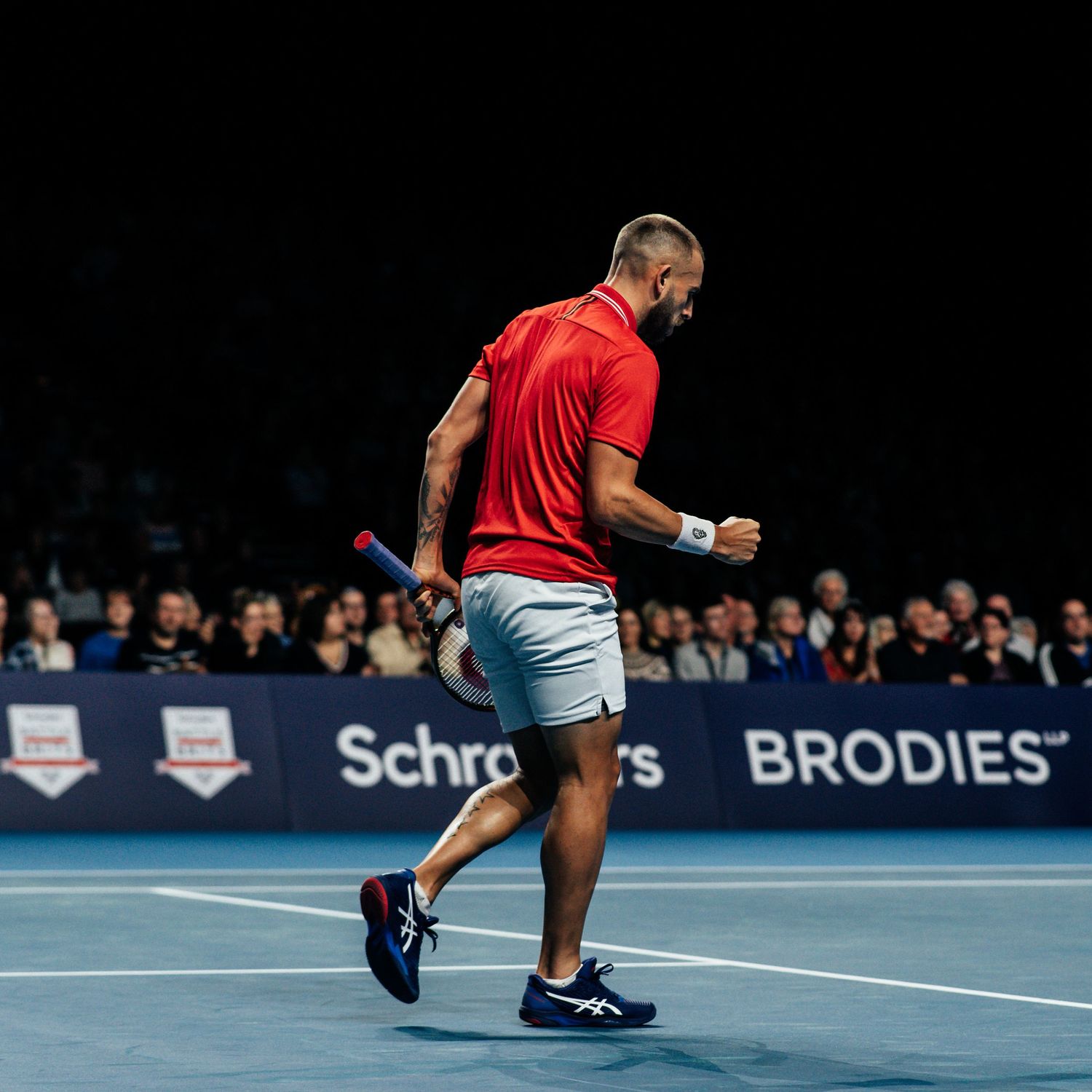 Tennis player in red shirt celebrating a point at a Schroders and Brodies sponsored match.