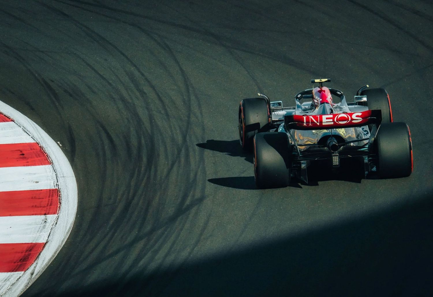 Mercedes INEOS F1 car racing on track, rear view showing aerodynamic details and tire marks on asphalt.