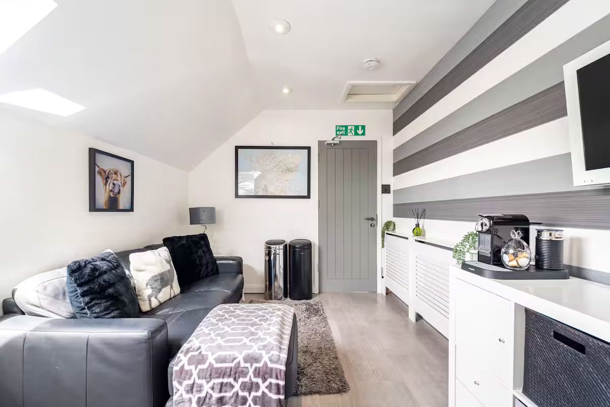 Cosy attic lounge with striped grey feature wall, black leather sofa, and white storage units.
