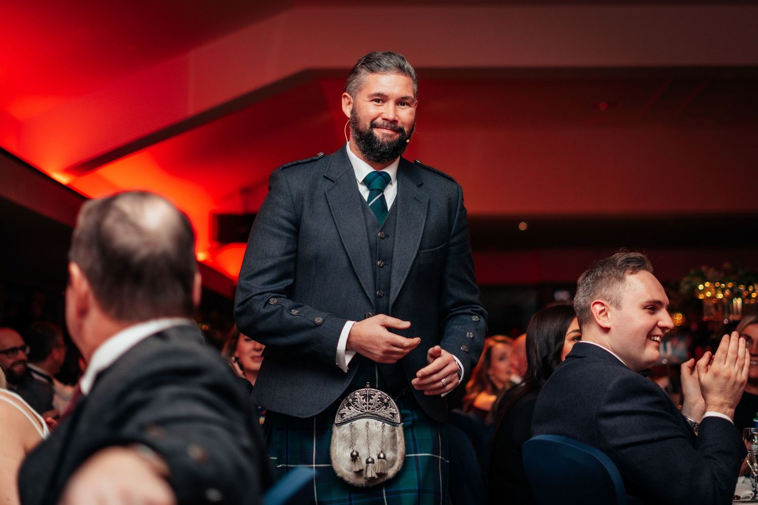 Smiling man in traditional Scottish kilt and jacket standing at a Burns Night celebration.