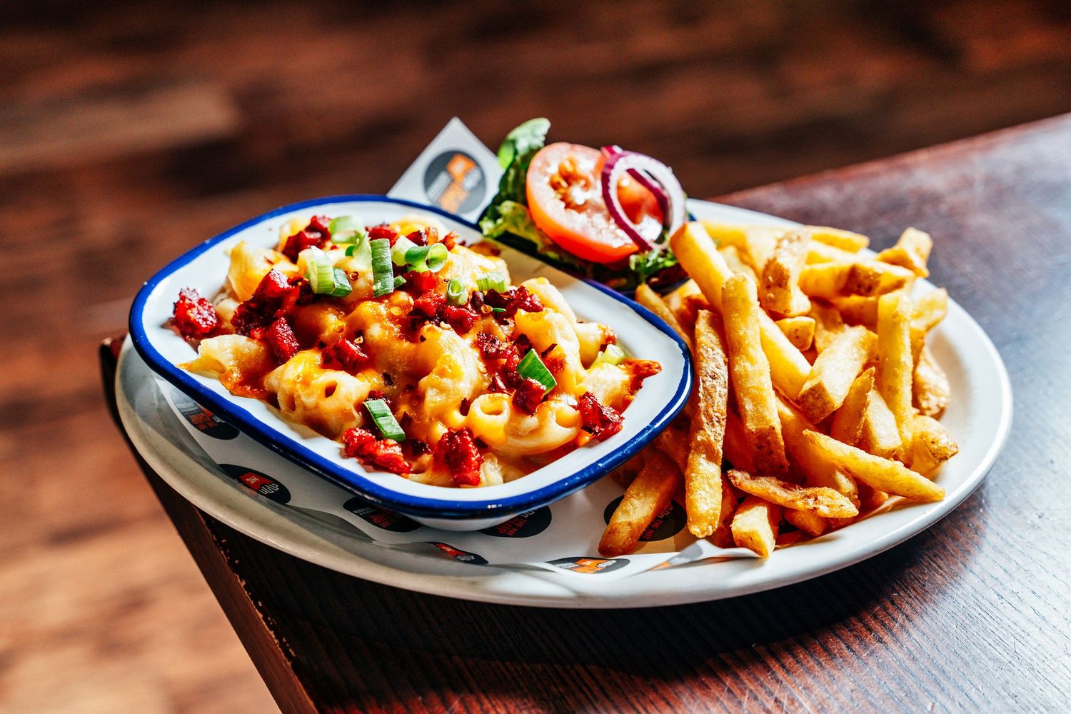 A plate of loaded mac and cheese with bacon and jalapeños served alongside crispy golden french fries.