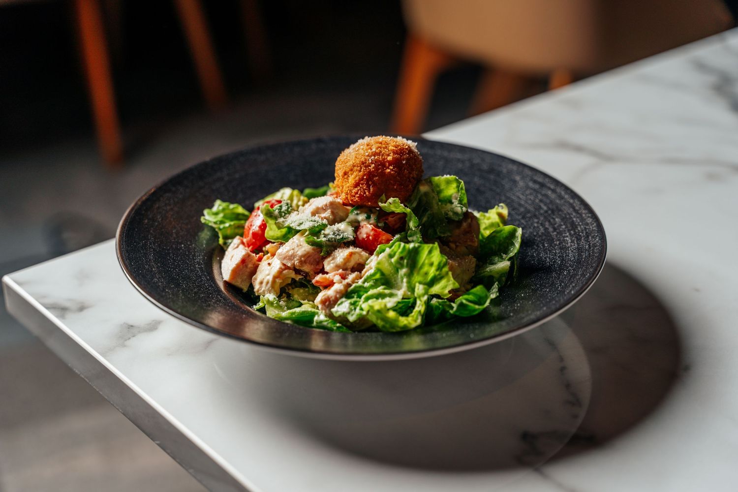 Gourmet salad with fried croquette, mixed greens, and vegetables served in a dark bowl.