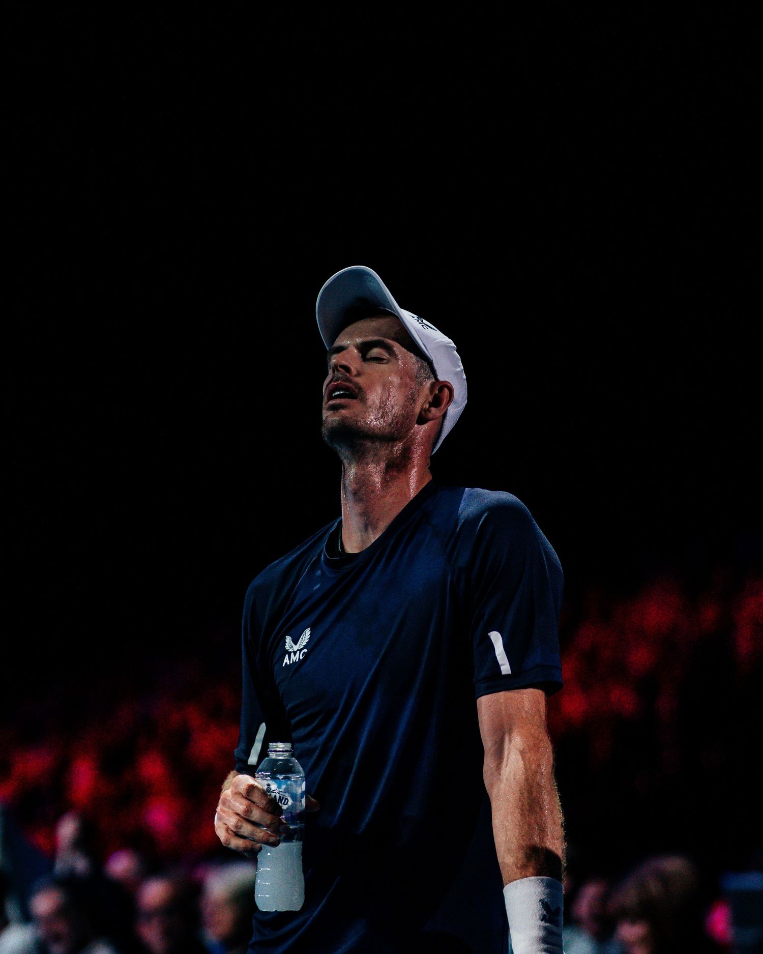 Close-up portrait of a tennis player holding a water bottle under dramatic indoor arena lighting.