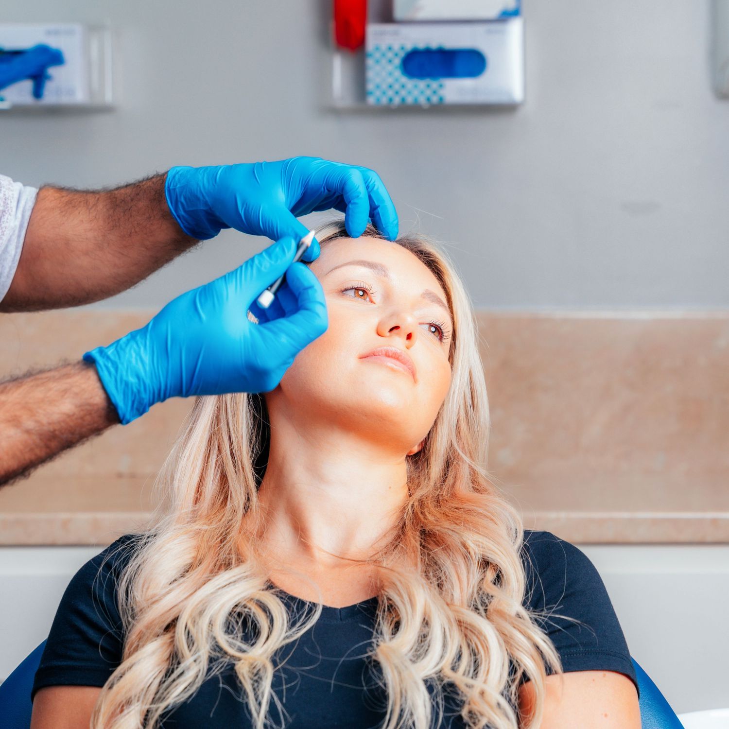 Medical professional in blue gloves administering a facial filler injection near a blonde woman's eye area.