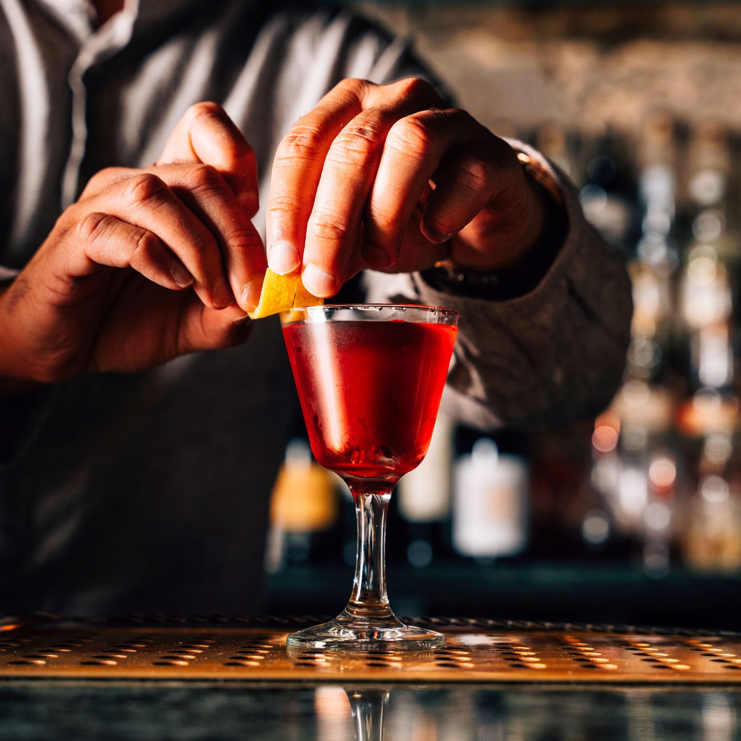 Bartender garnishing a classic red Negroni cocktail with an orange peel at a bar.