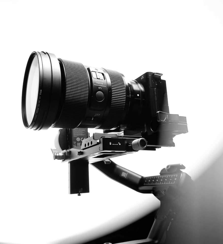Black and white photo of professional camera with telephoto lens mounted on stabilizer rig.