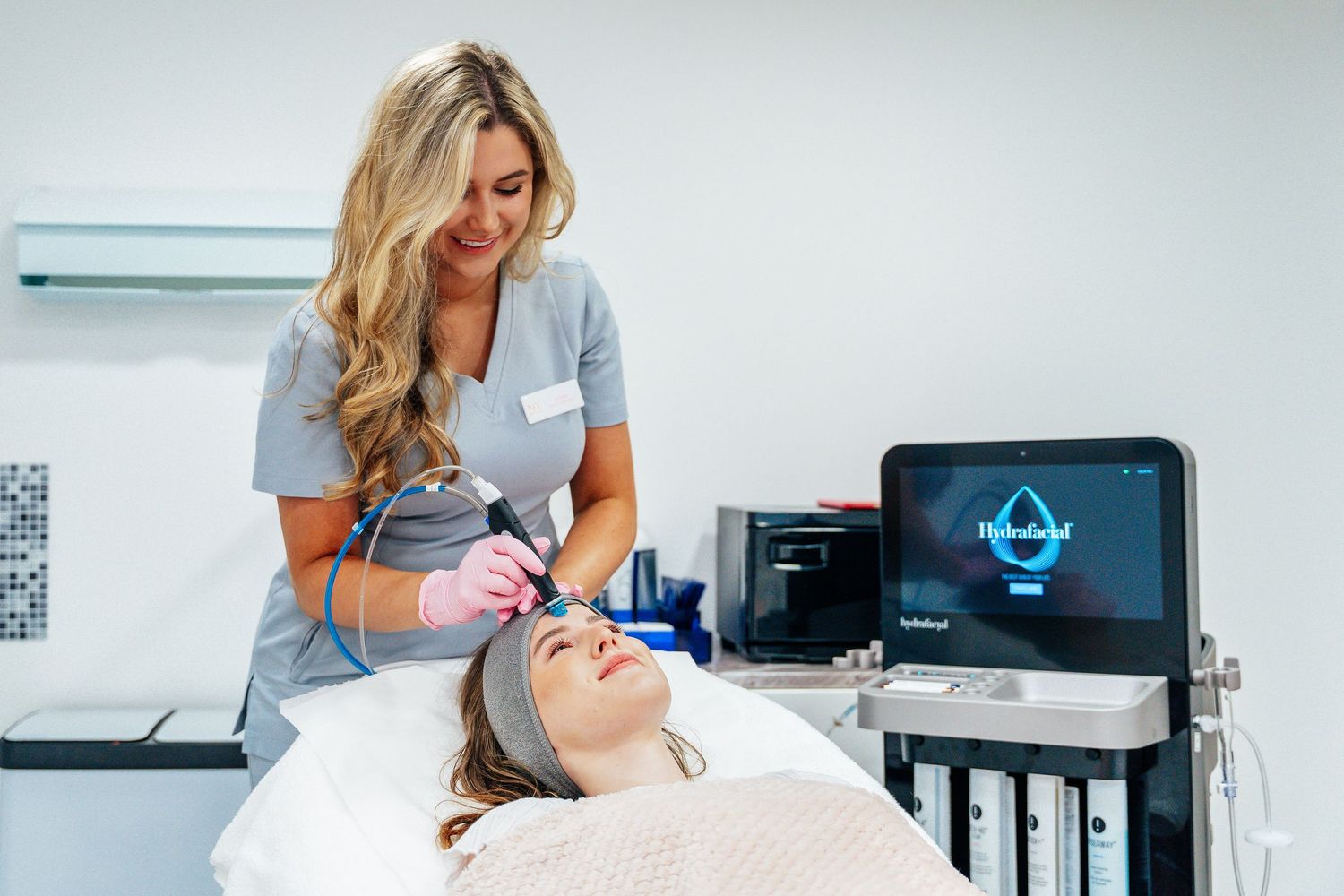 Aesthetic practitioner performing a HydraFacial treatment on a relaxed female client in a beauty clinic.