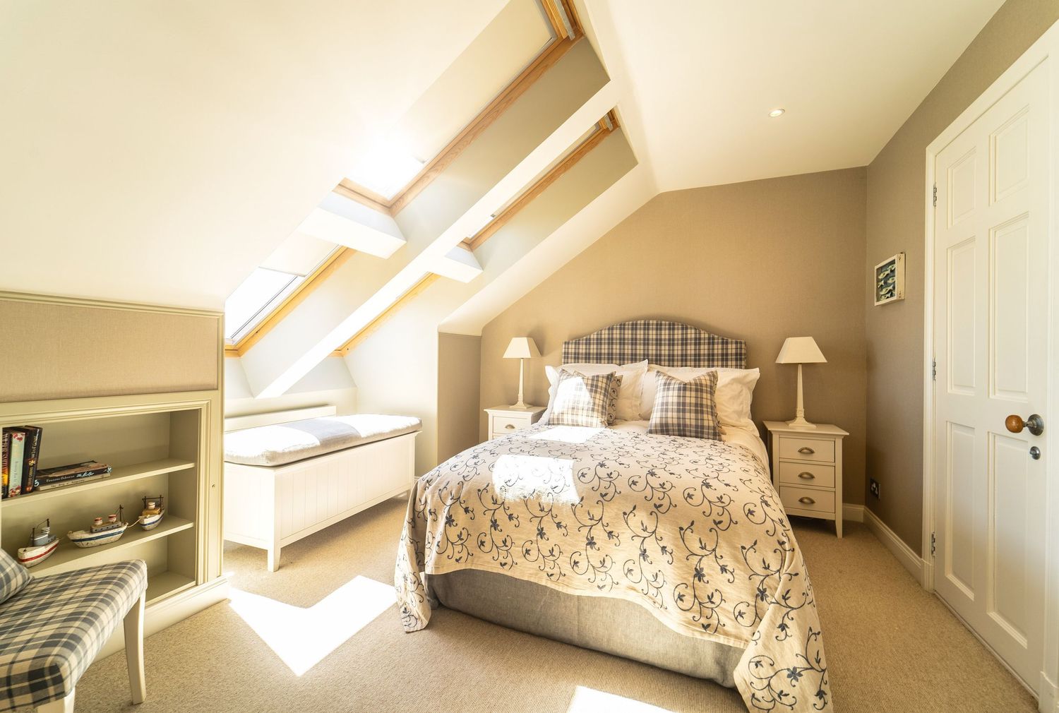 Cosy attic bedroom with Velux skylights, tartan headboard, twin bedside tables, and neutral decor.