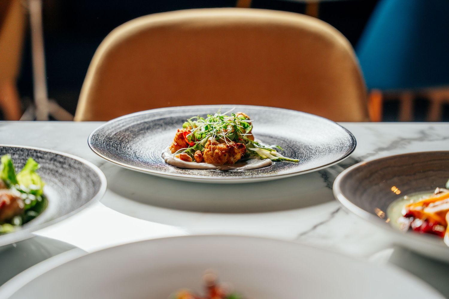 Fine dining plate with sauced protein and microgreens garnish on a marble restaurant table.