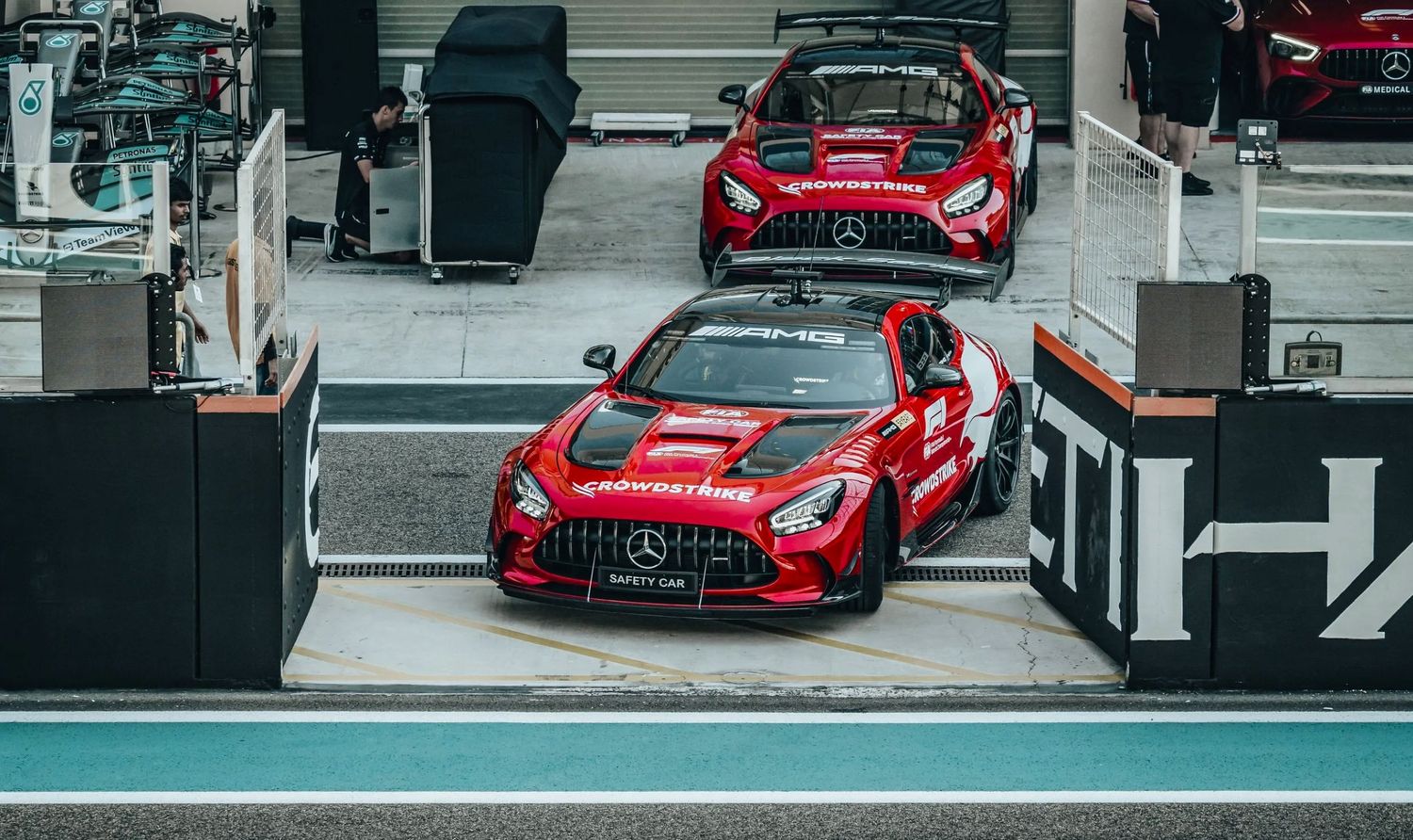 Two red Mercedes-AMG GT safety cars parked in the pit lane at a Formula 1 racing circuit.