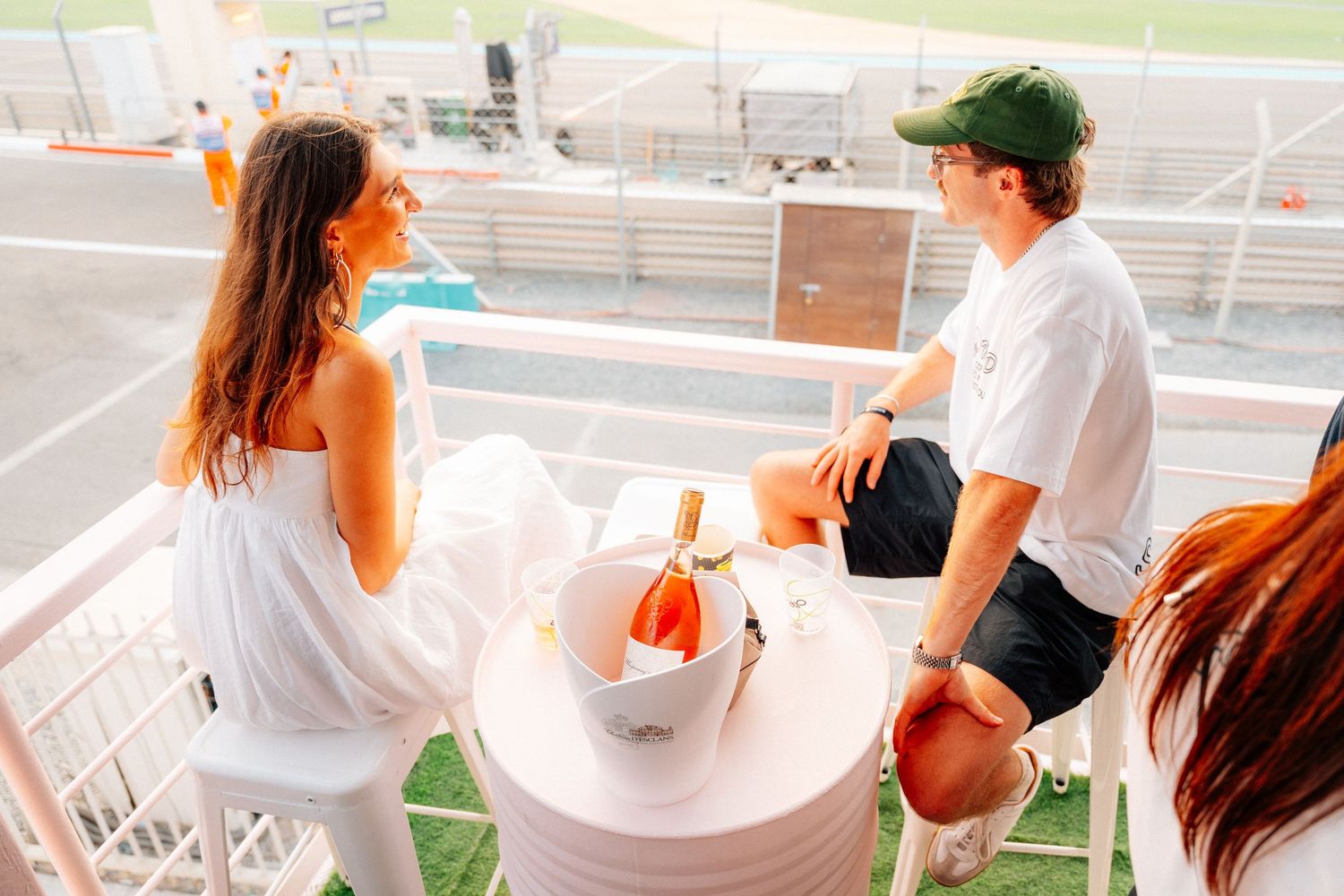 Couple sharing Whispering Angel rosé wine at a rooftop table overlooking a sunny racetrack venue.