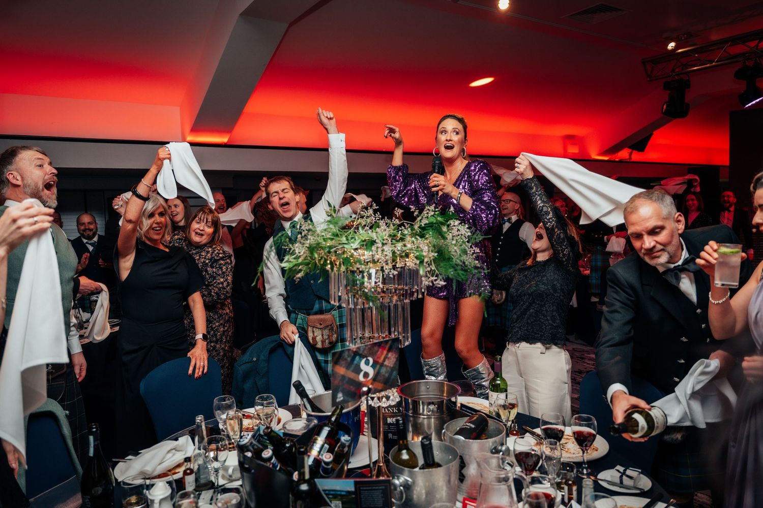 Excited guests waving napkins and celebrating at a festive Burns Night gala dinner table.