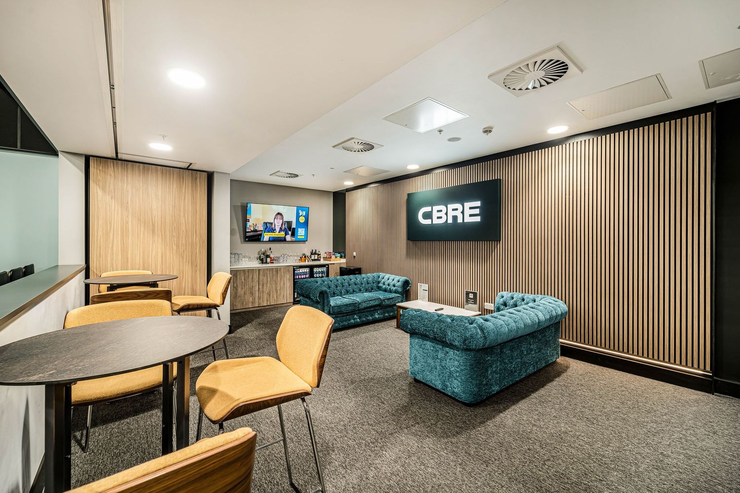 CBRE branded corporate lounge with teal Chesterfield sofas, wood panel walls, and flat screen TV display.