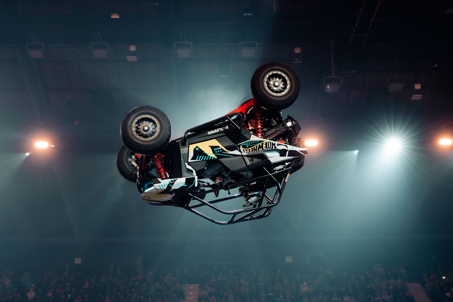 A colorful stunt car flips upside down mid-air under bright arena spotlights during a live show.
