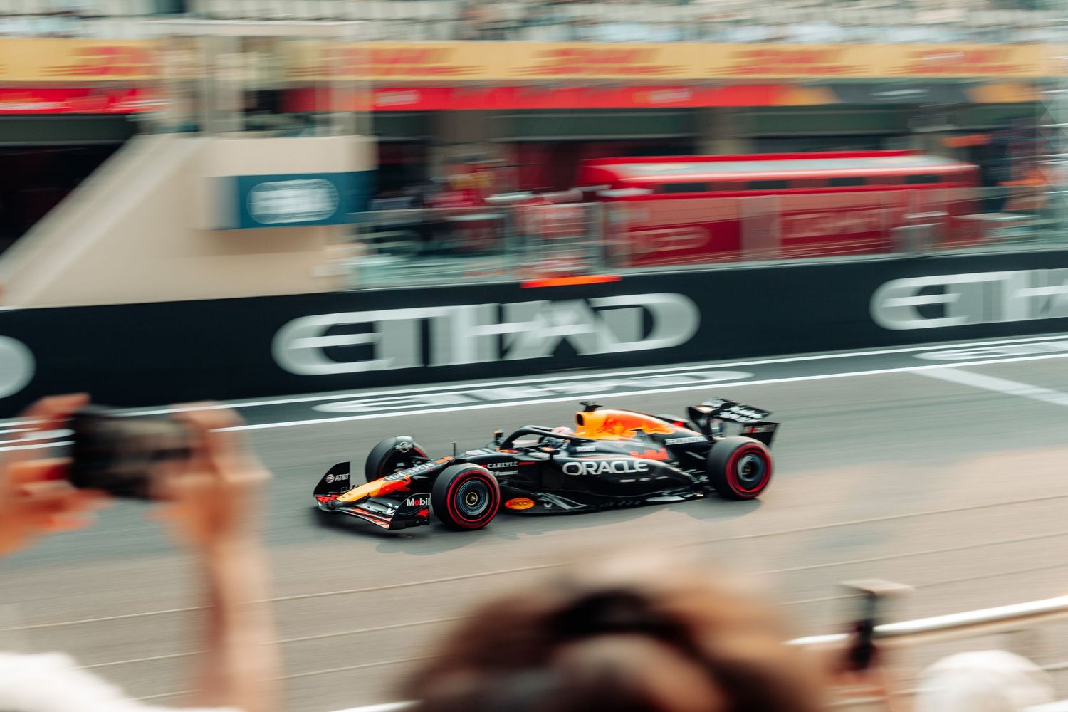 Red Bull Formula 1 car speeds past Etihad-branded barriers captured with motion blur effect.