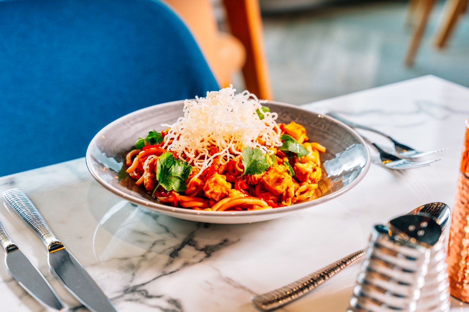 Pasta dish with tomato sauce, vegetables, and grated cheese in a bowl on a marble table.