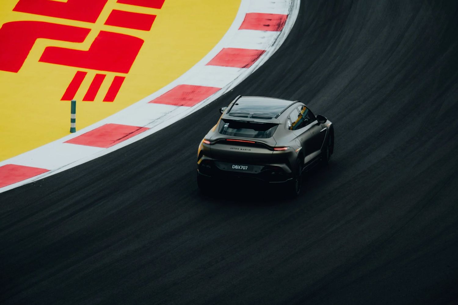 Black sports car navigating a curved race track with colorful barriers, captured from an aerial perspective.