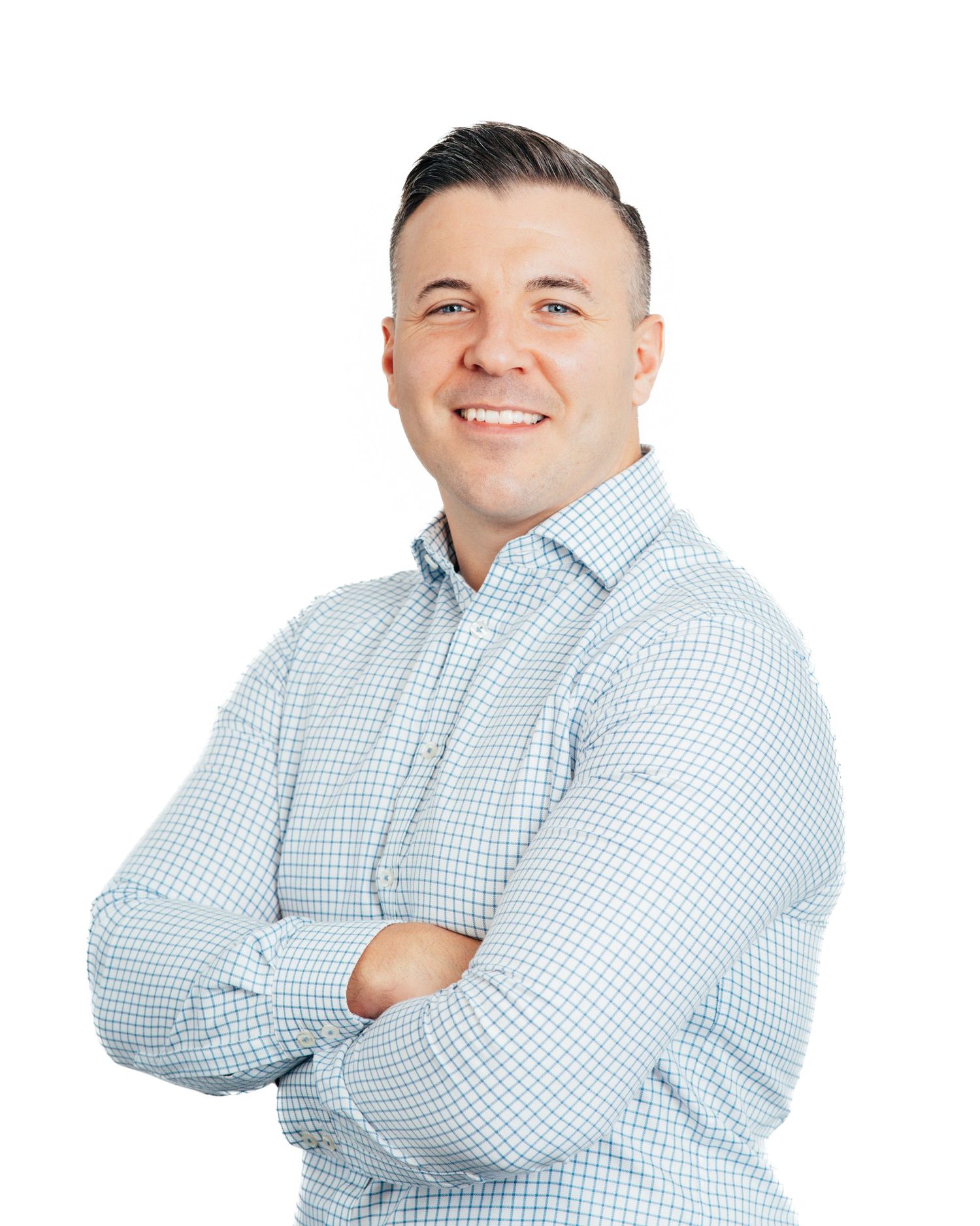 Smiling professional man in light blue checkered shirt standing with arms crossed against white background.