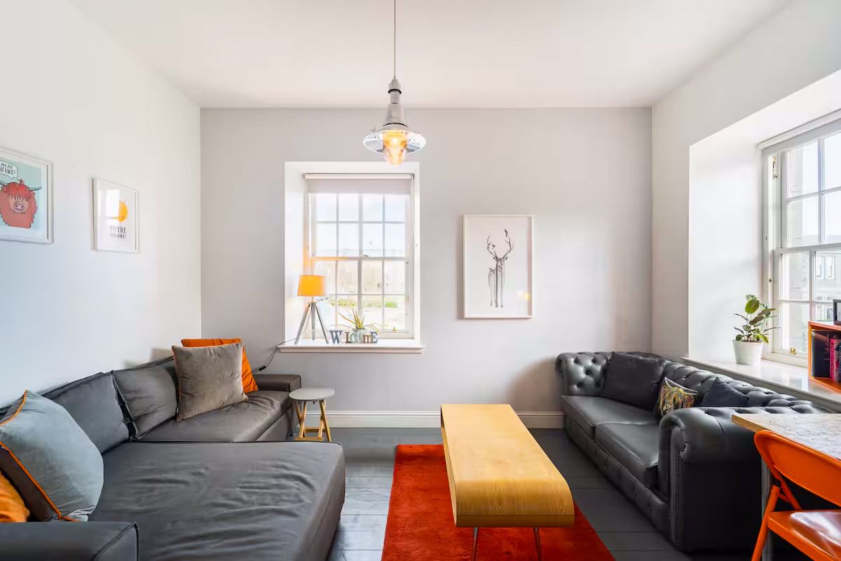 Bright living room with grey corner sofa, orange rug, pendant light, and white walls.
