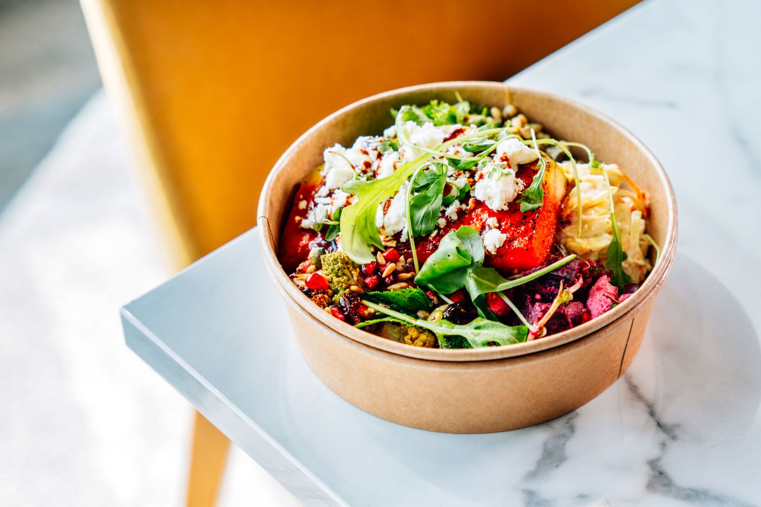 Colorful grain bowl with strawberries, greens, corn, and feta cheese in a kraft paper cup.