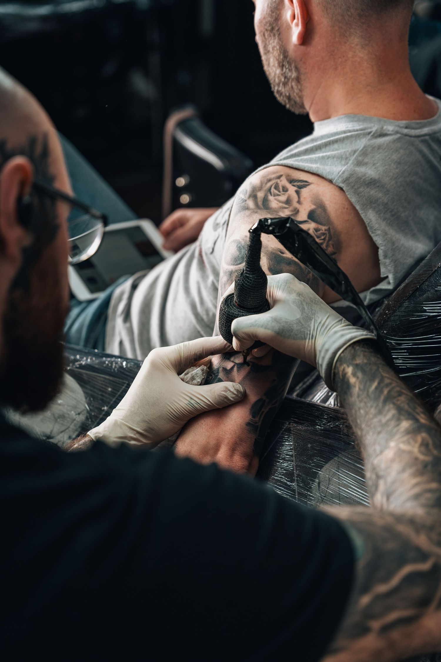 A tattoo artist in gloves working on a detailed arm tattoo in a professional studio.