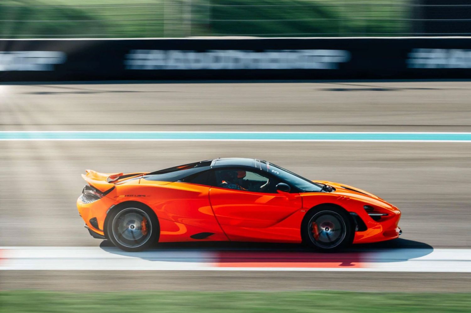 Orange McLaren 720S supercar speeding on a race track, captured in motion blur side profile view.