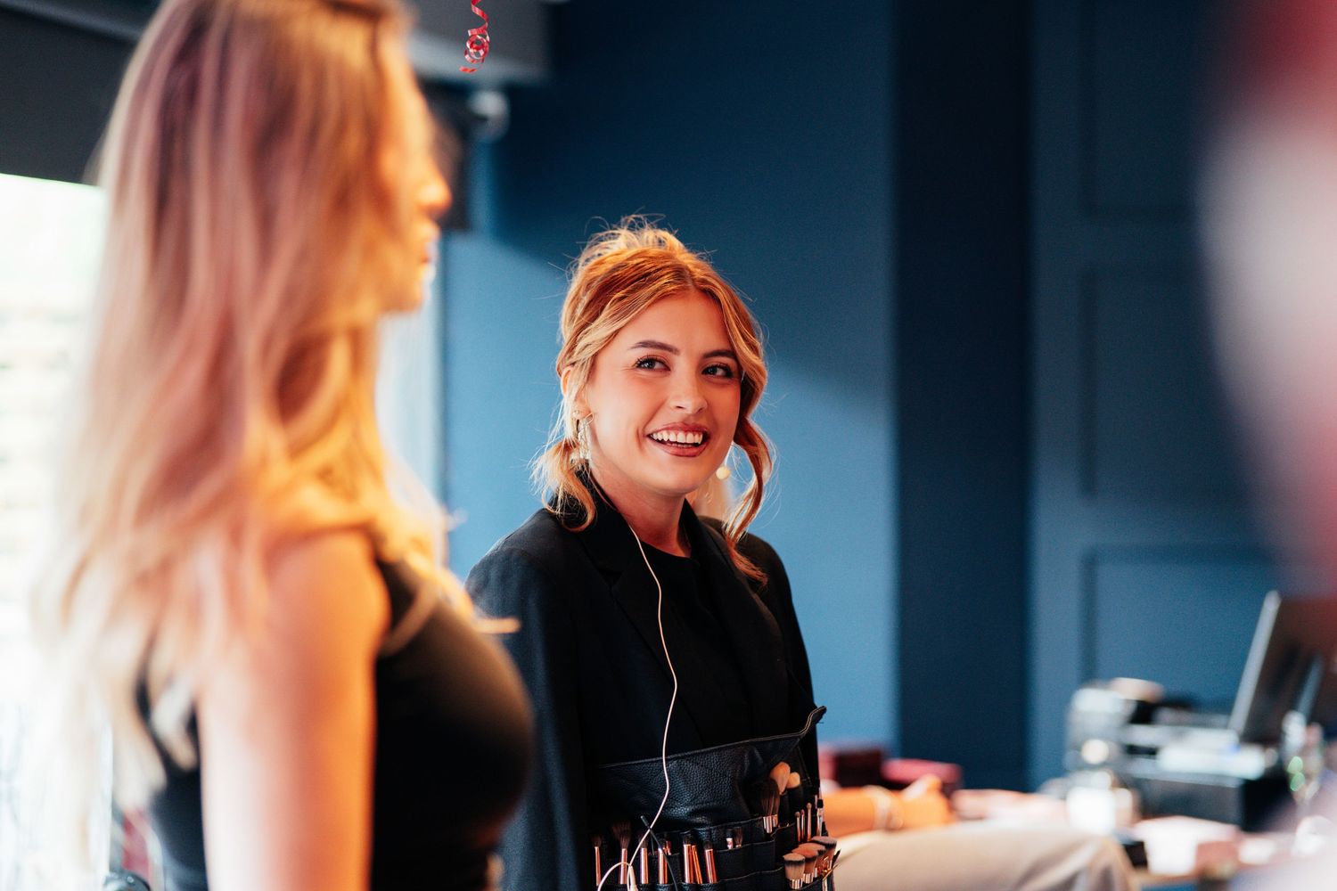 Smiling redhead woman in black outfit working at a reception desk in a modern blue interior.