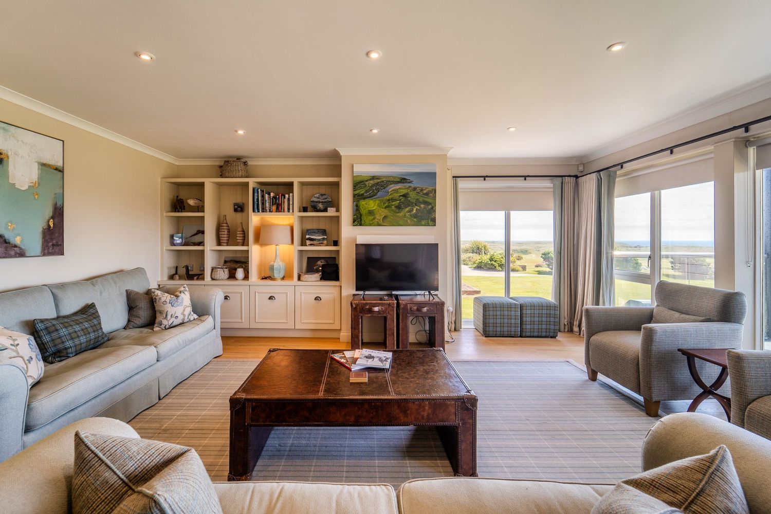 Elegant living room with cream built-in bookcase, flat screen TV, large windows, and neutral sofas.