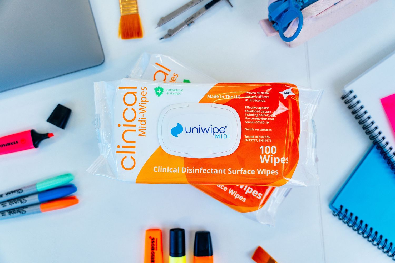 Uniwipe Clinical Disinfectant Surface Wipes 100-pack surrounded by colorful stationery on a white desk.