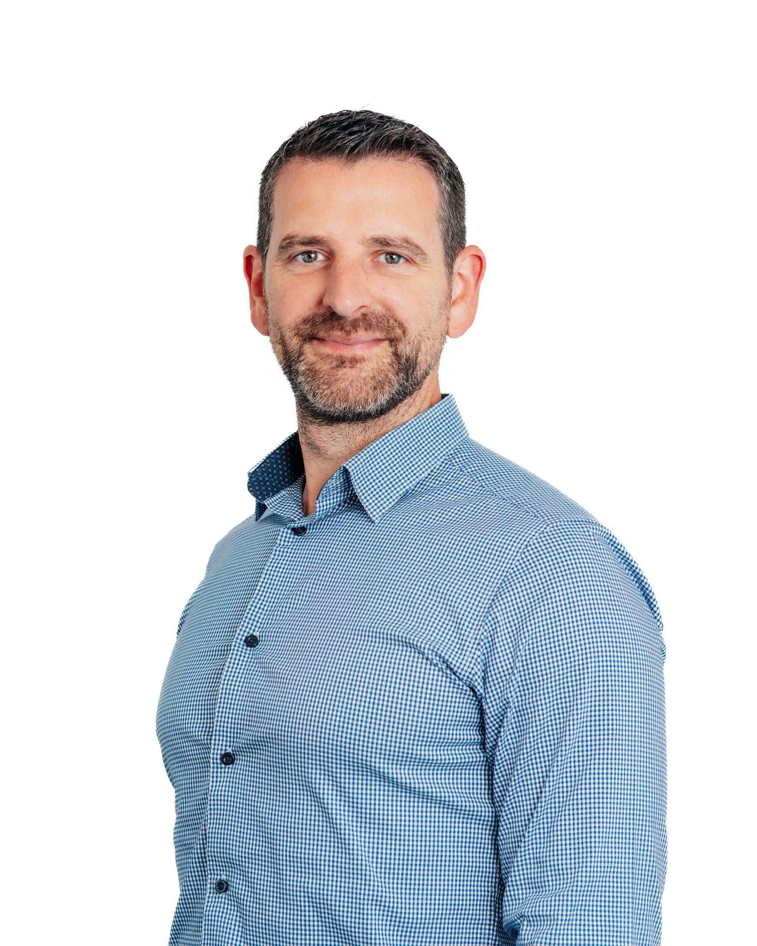 Smiling bearded man in blue checkered shirt posing against a clean white background.
