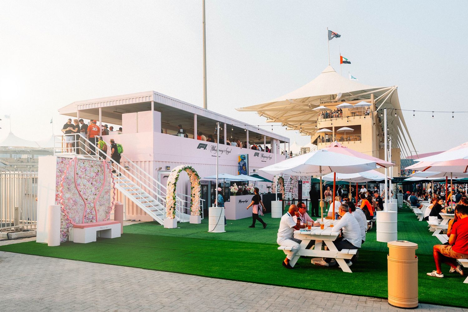 Outdoor event venue with white picnic tables on artificial grass at sunset.