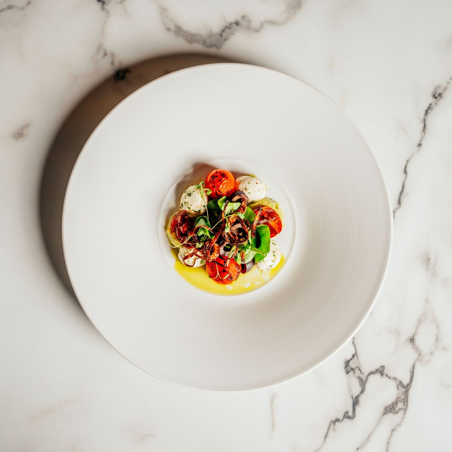 Elegant fine dining dish with roasted tomatoes and herbs on a white plate atop marble surface.