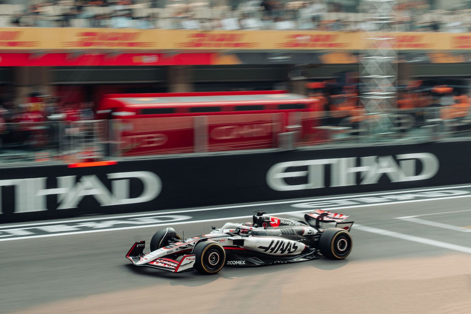 Haas F1 car speeding past Etihad Airways advertising boards at Abu Dhabi Grand Prix circuit.
