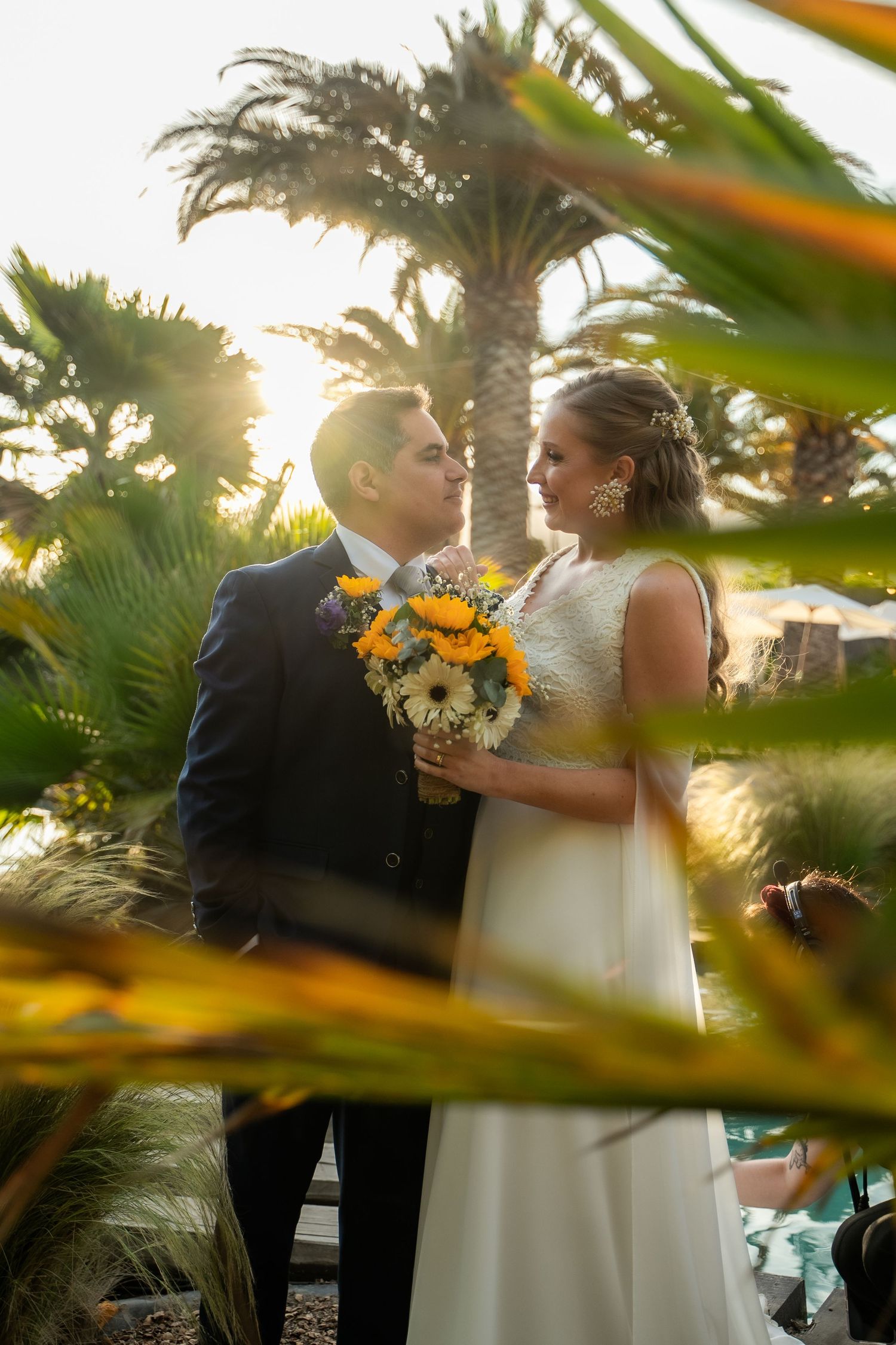 A tropical wedding portrait with palm trees and sunlight filtering through exotic foliage.