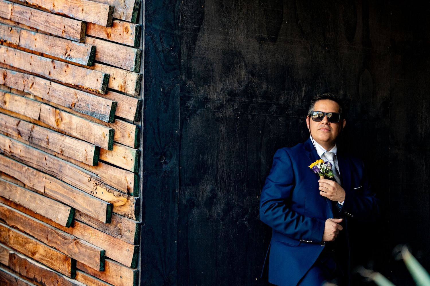 Person in a navy blue suit standing against exposed brick wall in dramatic lighting.