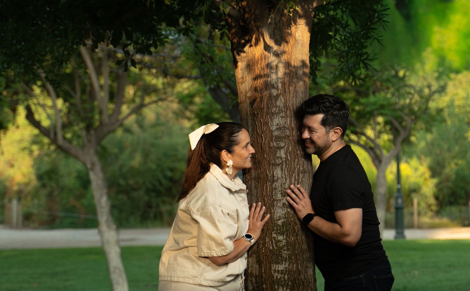 Playful wedding couple shares laughs while posing against trees in a green park.