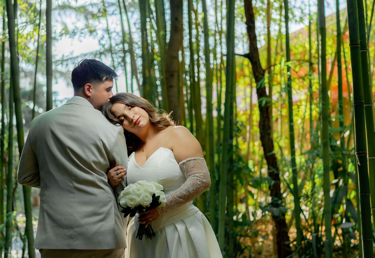 Newlyweds embracing in a lush bamboo forest, bride holding white bouquet.