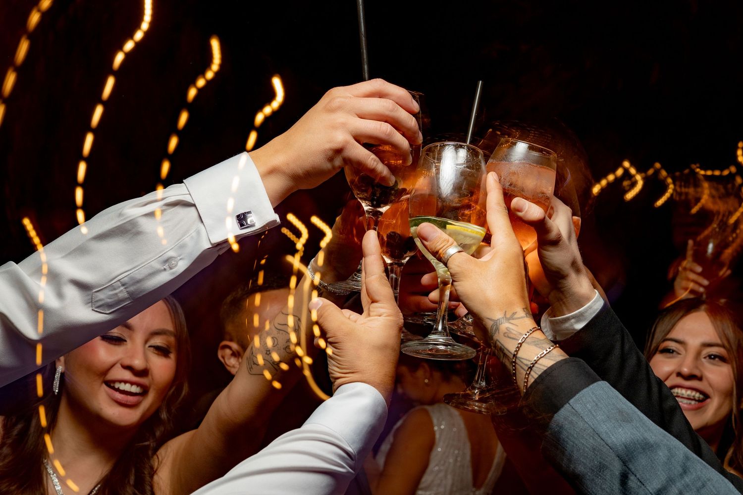 Group of smiling friends toasting with cocktails at a festive party with bokeh lights in the background.
