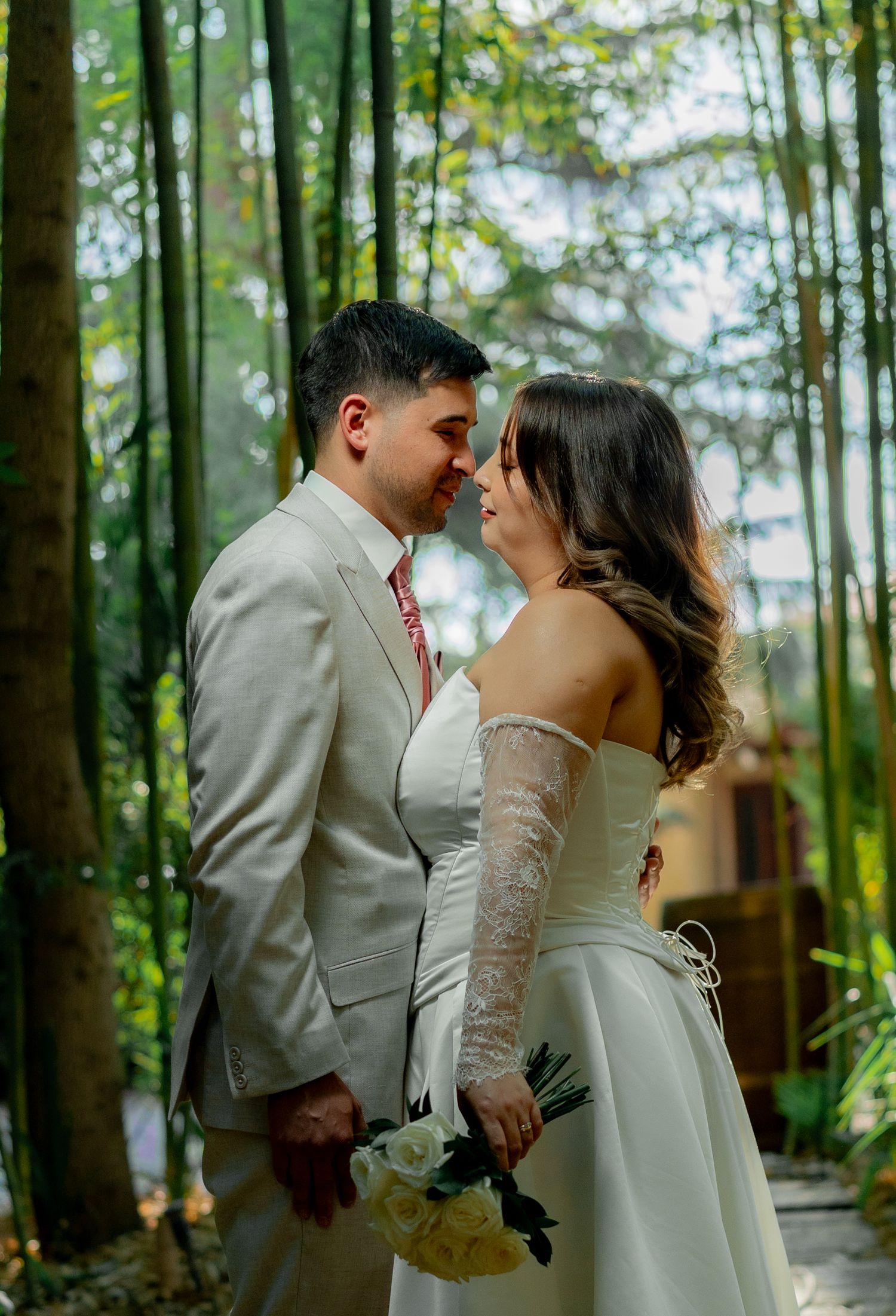 Couple in wedding attire sharing a romantic moment surrounded by lush green bamboo forest.