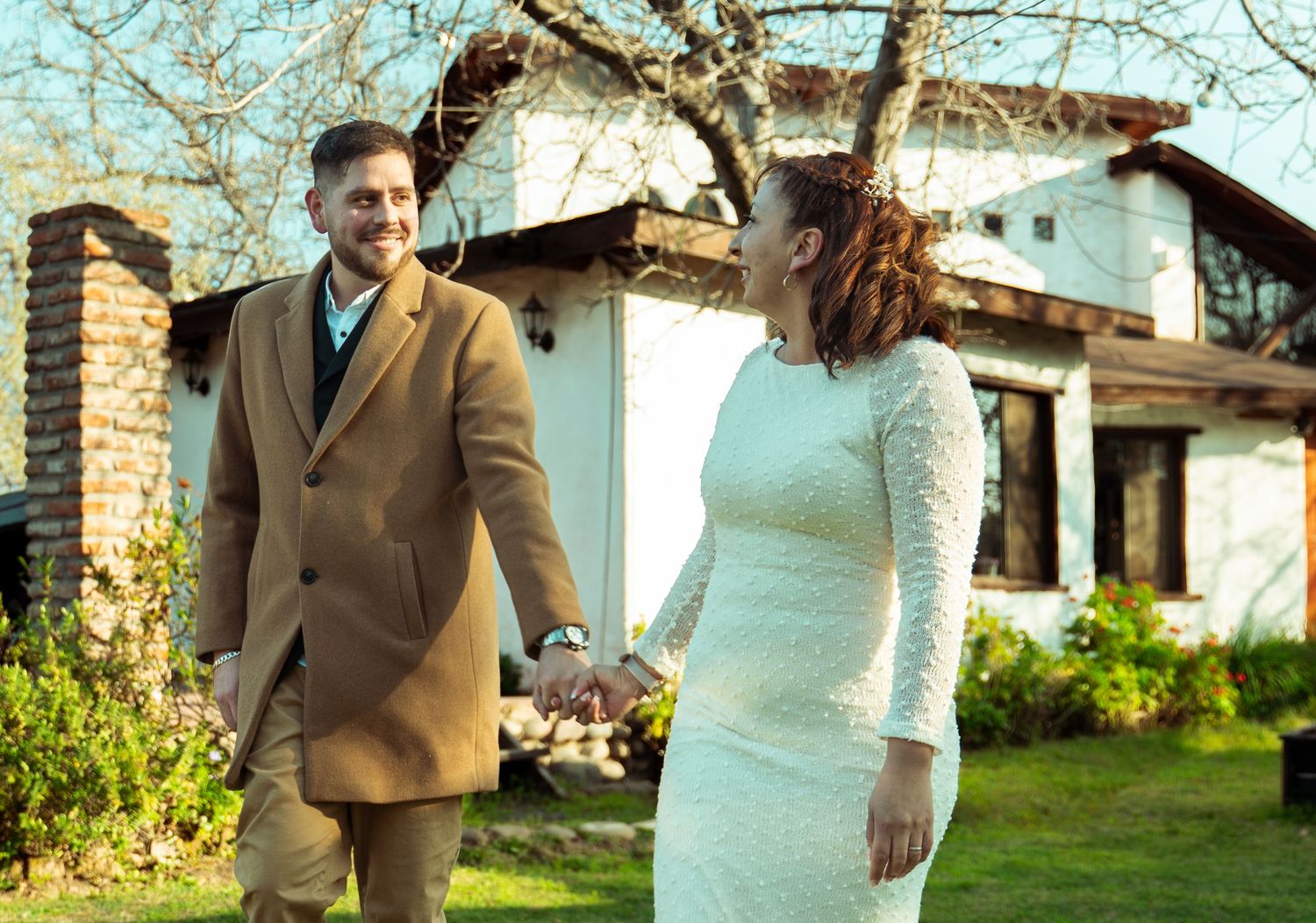 Wedding couple poses in front of rustic architecture and garden scenery.