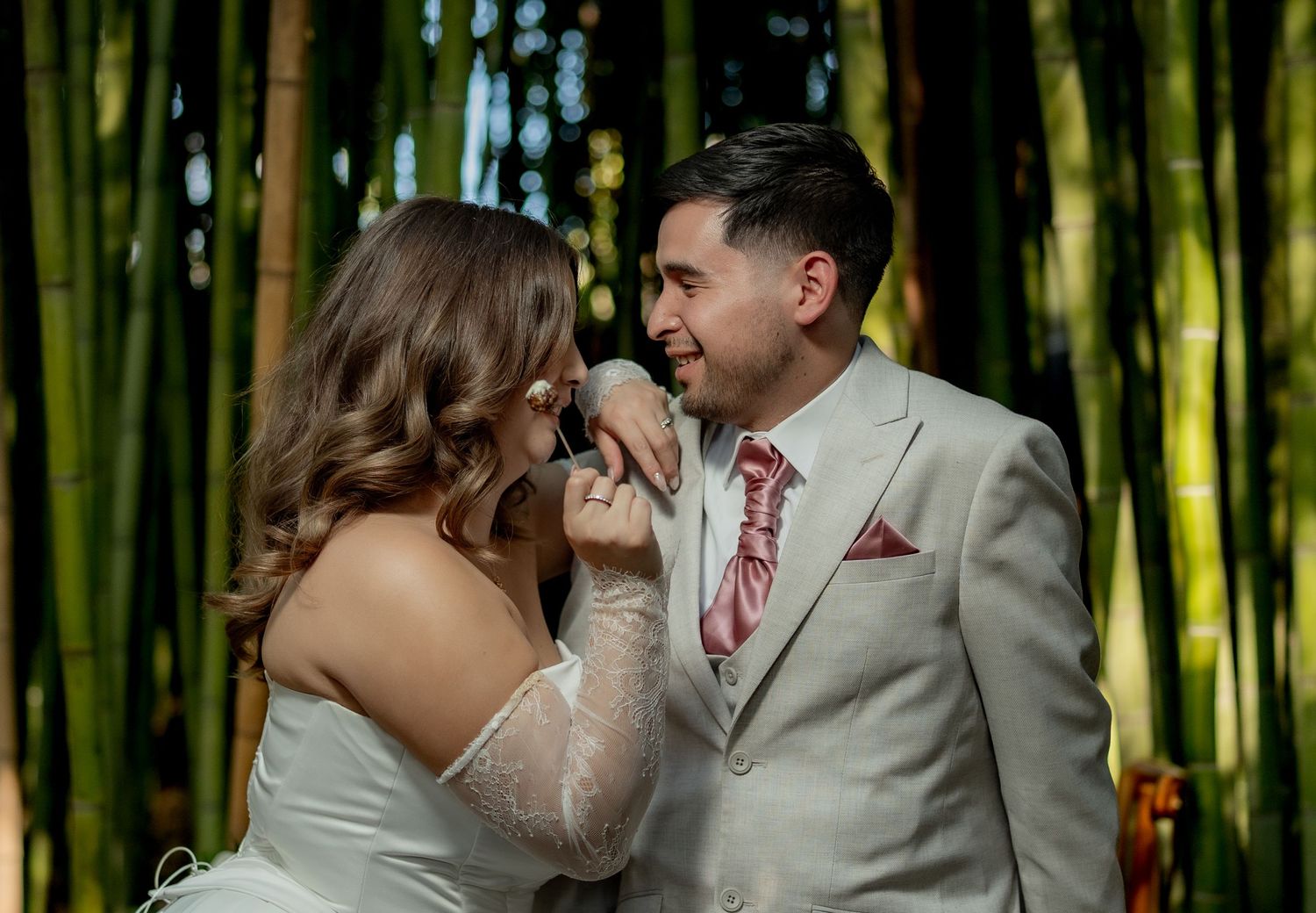 Bride and groom sharing tender moment surrounded by lush bamboo grove at outdoor wedding ceremony.