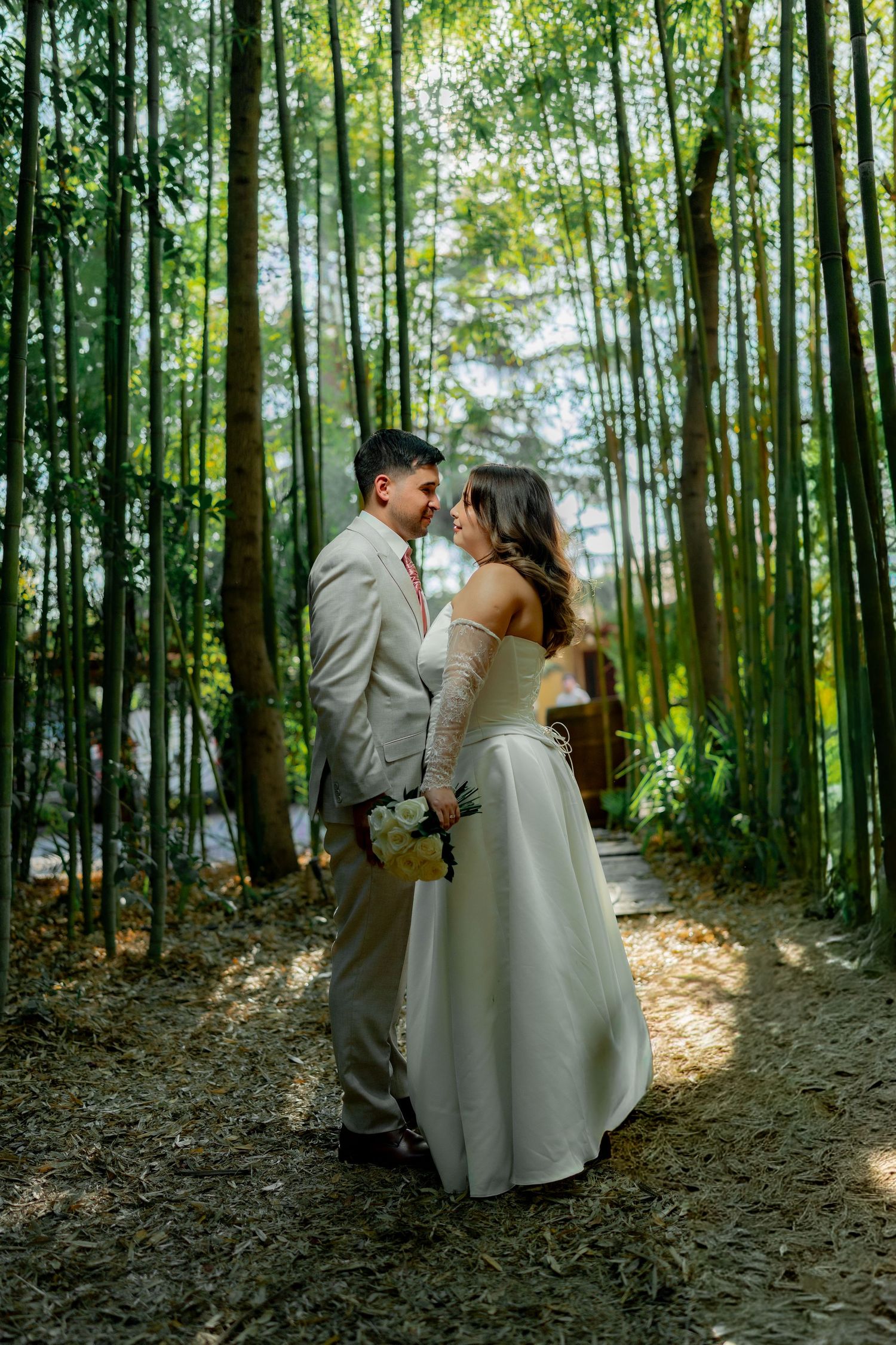 Bride and groom sharing romantic moment surrounded by tall bamboo trees outdoors.