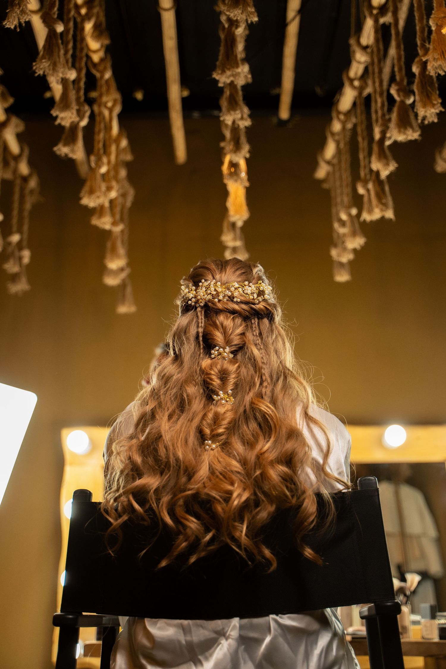 Back view of person with curled hair wearing delicate crown under ambient lighting.