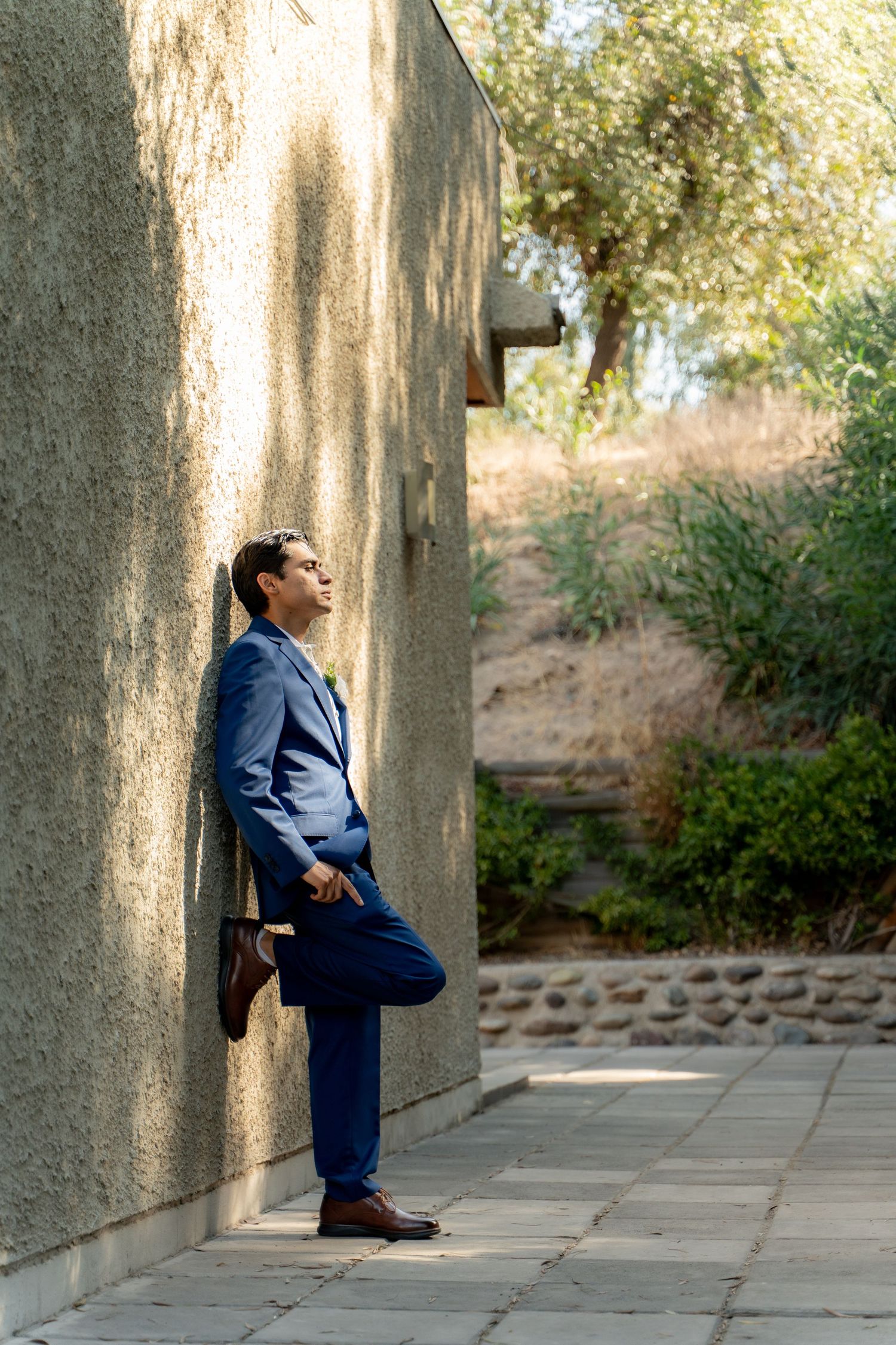 Person in navy blue suit leaning against concrete wall in outdoor setting during daytime.