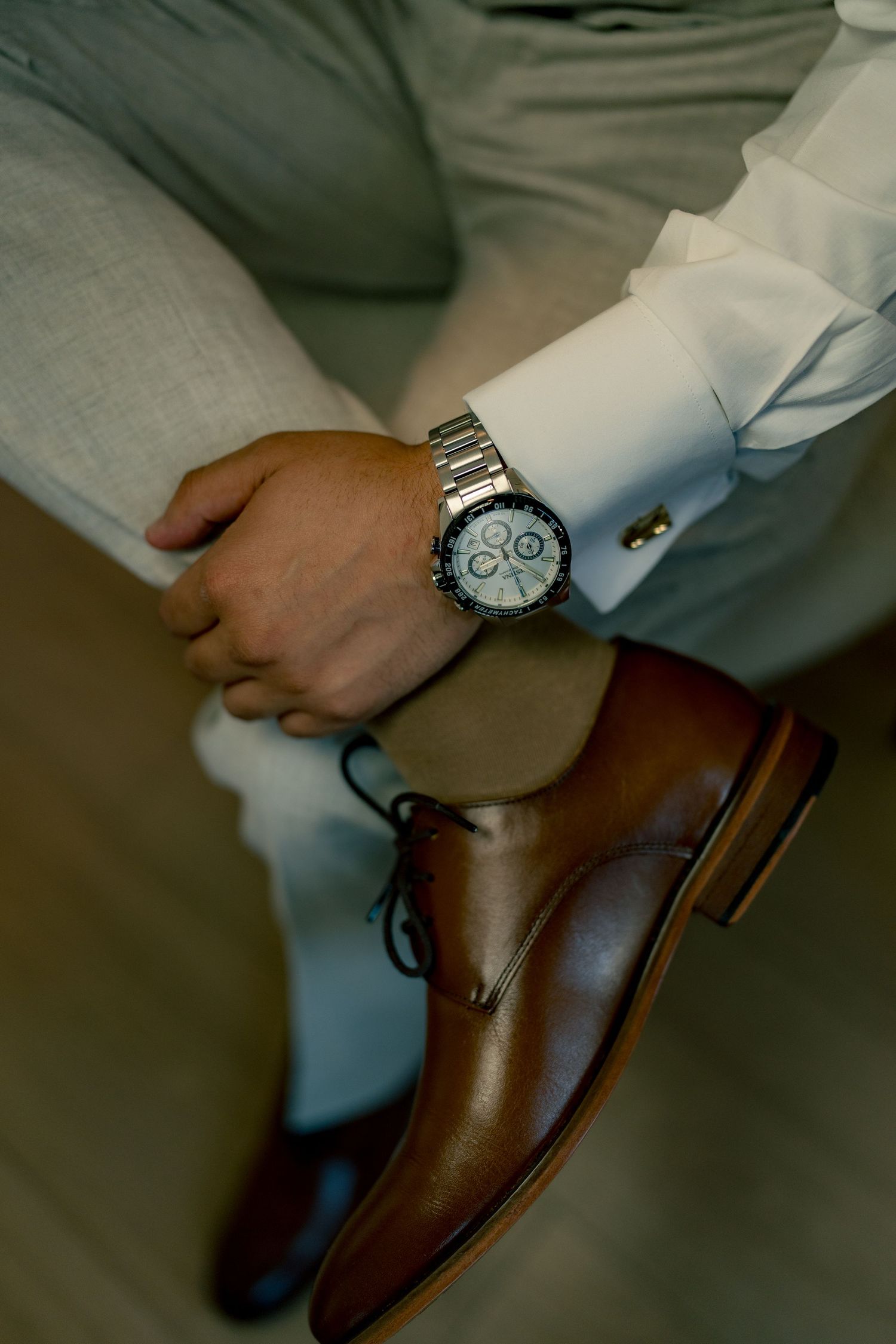Close-up of groom wearing silver chronograph watch, white dress shirt, and brown leather oxford shoes.