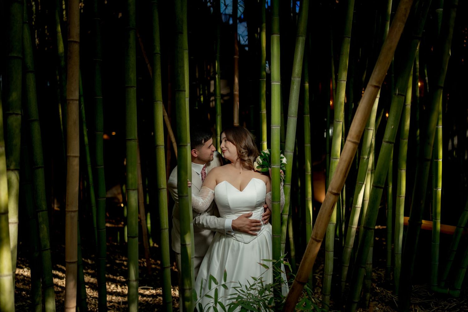 Romantic couple kissing among tall bamboo stalks in evening light.