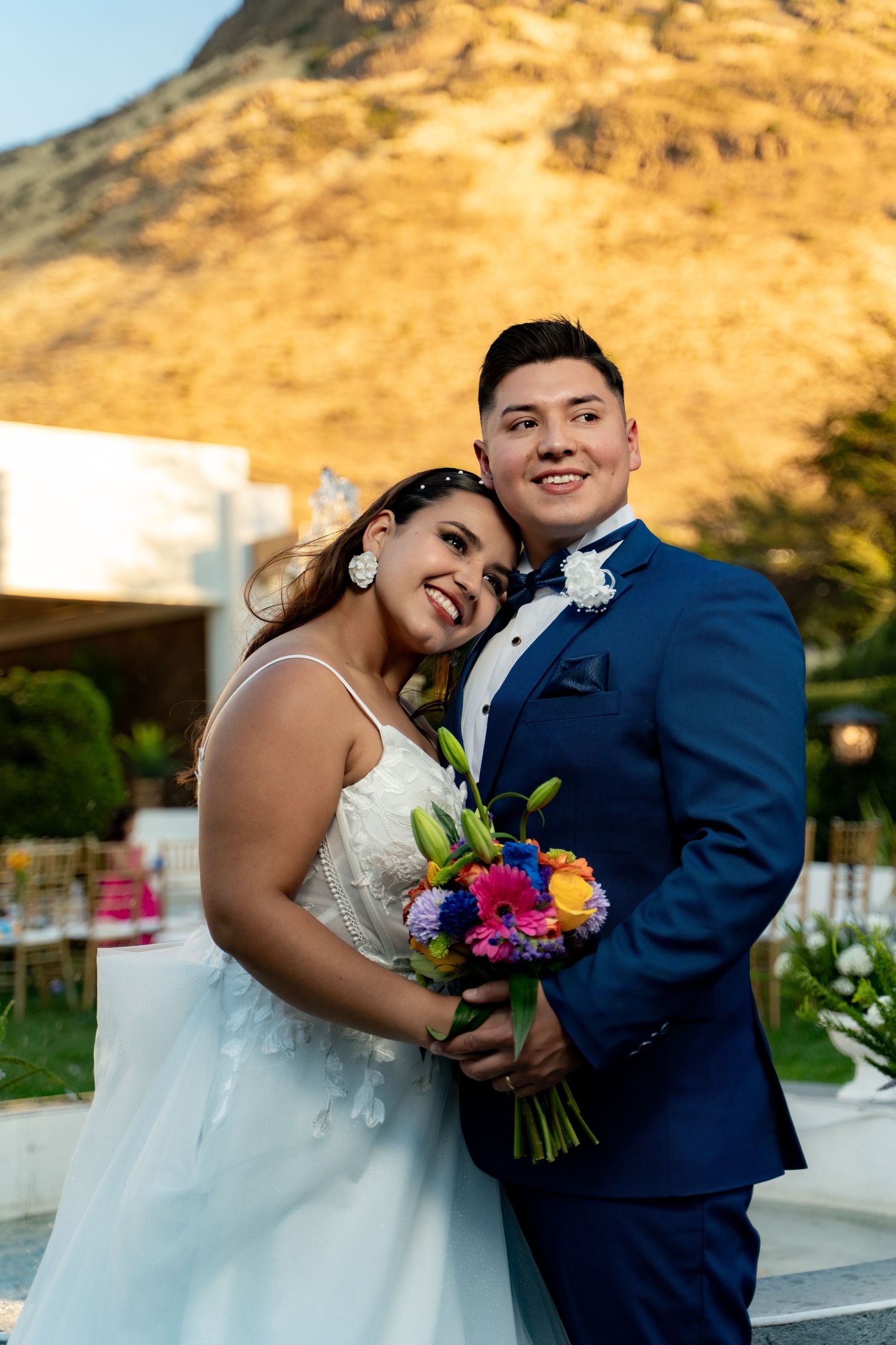 A couple poses for wedding photos against a golden mountain backdrop at sunset.