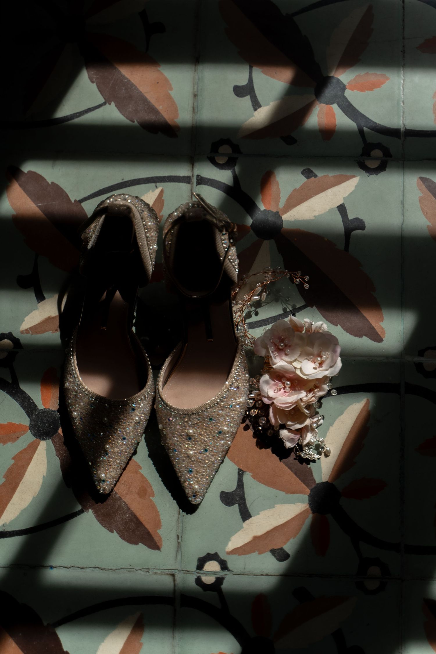 Sparkly wedding shoes and floral details on a patterned tile floor in dramatic lighting.