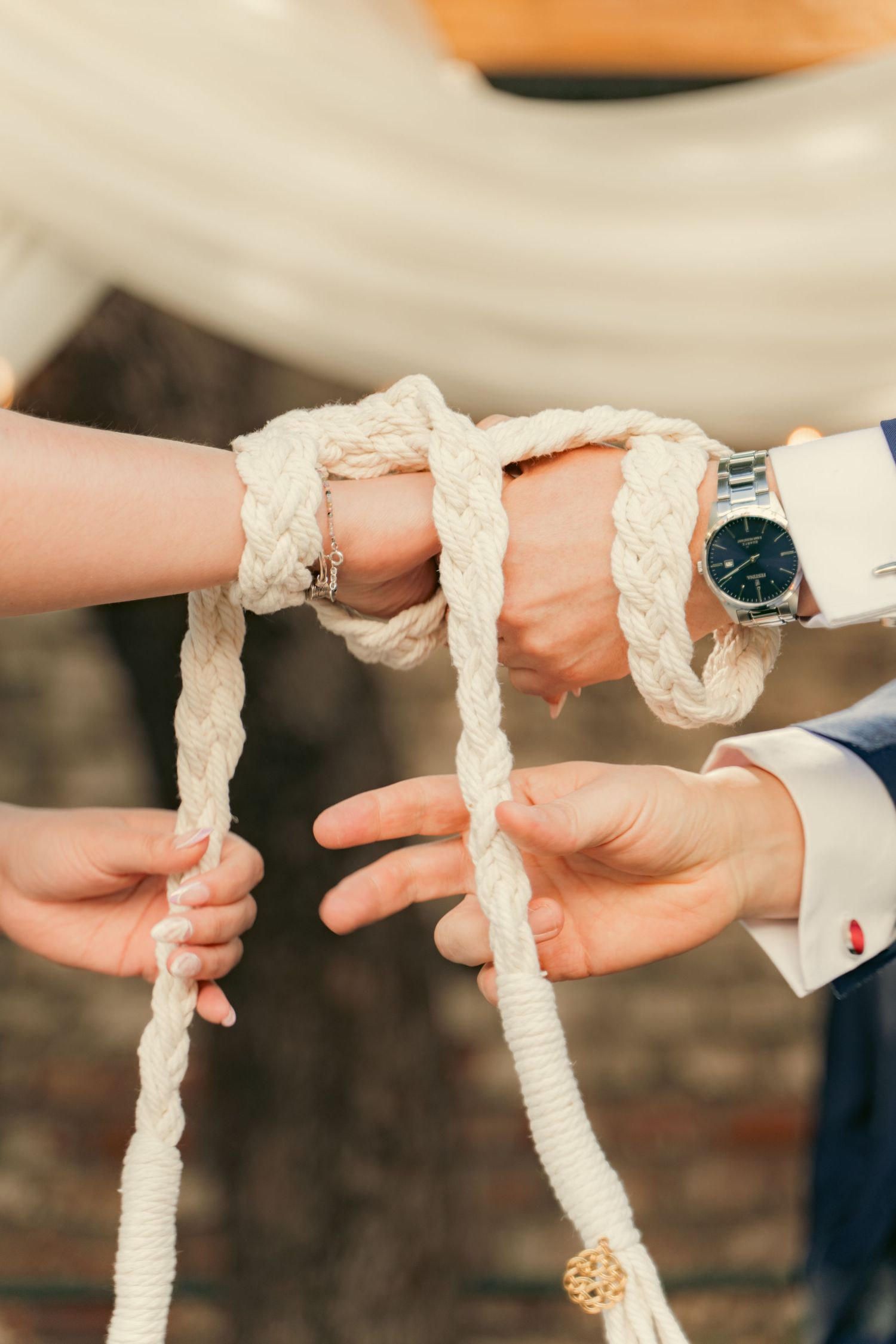 Close-up sequence showing hands holding a decorative white cord or rope during a traditional ceremony.